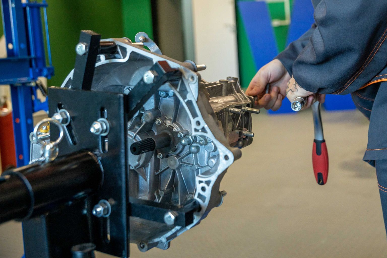 Mechanic uses tools to repair car transmission in an indoor workshop setting.